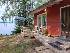 een rood huis met een veranda met stoelen en een parasol bij Lakeside Hilda, rantamökki 