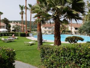 a pool with palm trees and people sitting in chairs at HG Jardín de Menorca in Son Bou