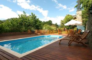a swimming pool with chairs and an umbrella on a wooden deck at Cabañas La Encantada in San Martín de los Andes