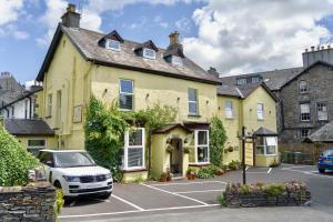 een geel huis met een auto geparkeerd op een parkeerplaats bij The Cottage in Windermere