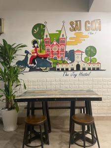 un tavolo con sgabelli di fronte a un muro con un murale di JOY HOSTEL ad Ho Chi Minh