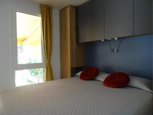 sypialnia z łóżkiem z czerwonymi poduszkami i oknem w obiekcie Camping Santin w Cavallino-Treporti