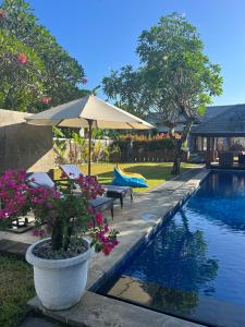 a swimming pool with chairs and an umbrella and flowers at Villa Tiller 2 in Lembuak