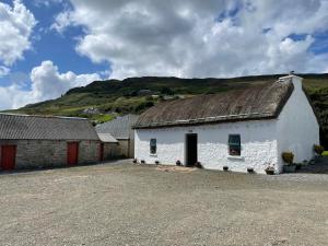 a white building with a roof with a hill in the background at Anne’s Thatched Cottage in Kilcar