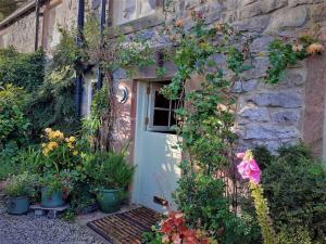 a stone house with a white door and some plants at Gorgeous romantic cosy cottage retreat with views in Winster