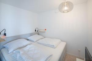 a white bed with white pillows and a light at FEWO Ferienresidenz Staberdorf Haus 76 Wohnung Nr 26 in Staberdorf