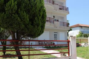 a white house with a red fence and a tree at Kondylenia Rooms in Loutrá Vólvis