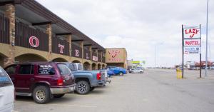 Lazy J Motel في Claresholm: موقف للسيارات مع وقوف السيارات أمام موتيل