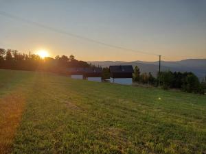a field with the sun setting behind a house at Domki Blisko Nieba III in Wisła