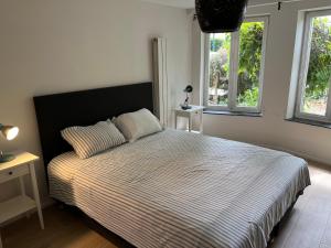 a bedroom with a bed with a striped comforter and two windows at Uccle Chic Flat in Brussels