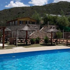 a swimming pool with tables and umbrellas in front of a house at Cabañas Gemas del Lago in Potrero de los Funes