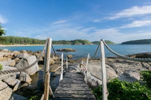 un puente de madera sobre un cuerpo de agua en Naiharn On The Rock Resort Phuket, en Nai Harn Beach