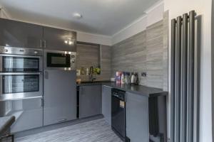 une cuisine équipée d'appareils en acier inoxydable et de placards gris dans l'établissement 5 Bedroom 5 Bath sleeps 10 close Luton Airport M1, à Caddington