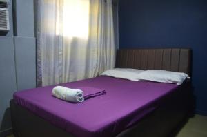 Una cama morada con una toalla enrollada encima en Gaius Inn, en Manila