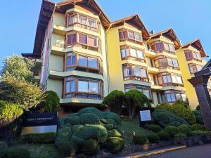 格拉玛多Suíte no Wish Resort Centro de Gramado的一座黄色的大建筑,有一堆灌木丛