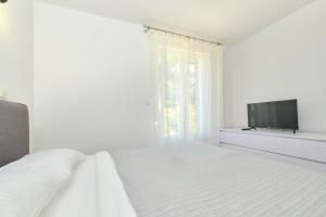ein weißes Schlafzimmer mit Bett und Flachbildfernseher in der Unterkunft Apartment Nora in Mali Lošinj
