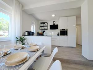 a white kitchen with a dining table and chairs at Holiday house SeaDream - 50 meters from the sea in Brodarica