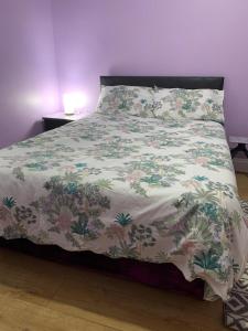 a bed with a flowered comforter on it with a table at Your Perfect HomeStay in Ilford