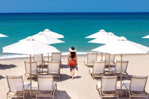 a woman walking on a beach with chairs and umbrellas at Calla Luxury Seafront Suites in Rethymno