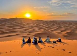 a group of people sitting in the desert watching the sunset at Bivouac Camel Trips in Merzouga