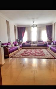 a living room with purple couches and a rug at Résidence al massirra in Fnidek