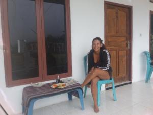 una mujer sentada en una silla junto a una mesa en Rice field guest house en Kelimutu