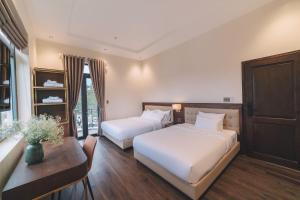 Cette chambre comprend deux lits, une table et un bureau. dans l'établissement Sunset Hill Dalat, à Đà Lạt