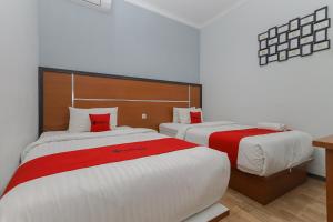 two beds in a hotel room with red and white sheets at RedDoorz Plus At Swun Stay Raya Langsep in Malang