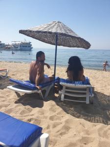 two people sitting on the beach under an umbrella at Sevo Hotel in Ayvalık