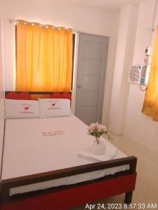 WJV INN MARIBAG0 في Maribago: غرفة مع سرير مع إناء من الزهور عليه