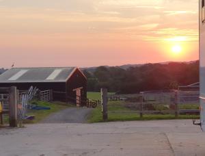 a red barn with the sunset in the background at Knapp Farm Glamping Lodge 2 in Corscombe