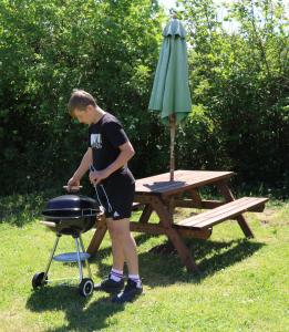 a man standing next to a grill and an umbrella at Knapp Farm Glamping Lodge 1 in Corscombe