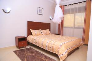 1 dormitorio con 1 cama y mesita de noche junto a una ventana en The Junction Apartments, en Mbarara