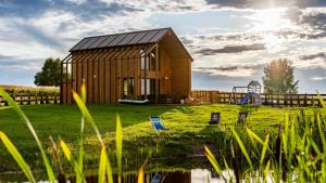 ein Holzhaus mit einem Metalldach neben einem Teich in der Unterkunft Apartamenty Sun & Snow Sielska Stodoła z sauną in Trękus