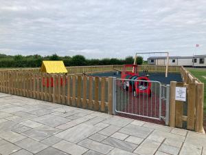 a wooden fence with a play park with a playground at Chapel Fields Holiday Park in Chapel Saint Leonards