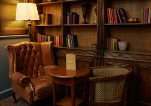 una silla y una mesa en una habitación con libros en Cock Hotel by Greene King Inns en Stony Stratford