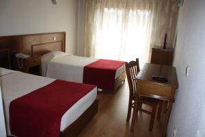 a hotel room with two beds and a desk and a window at Hotel Classis in Bragança