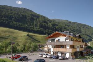 a building with cars parked in a parking lot in front of a mountain at Hotel Bergland in Cadipietra