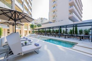 uma piscina exterior com mesas e cadeiras e um guarda-sol em Divani Escape em Atenas