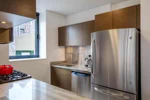 a kitchen with a stainless steel refrigerator and wooden cabinets at Midtown 1BR w Pool Gym Parking nr Times Sq NYC-378 in New York