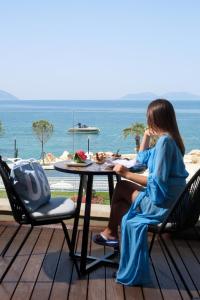 una mujer sentada en una mesa frente al océano en Priam Hotel Luxury Resort, en Vlorë
