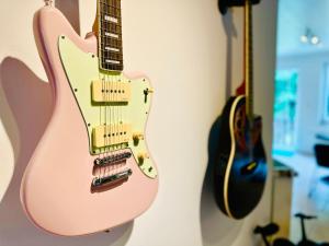 una guitarra rosa colgada en una pared con otras guitarras en La maison du Groove, en Trois-Ponts