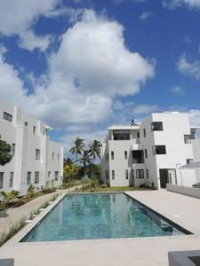 a swimming pool in front of two white buildings at CAPLAGE - BEACHFRONT GROUND FLOOR APARTMENT in TAMARIN in Tamarin