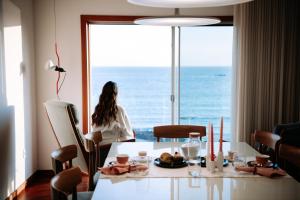 a woman sitting at a table in front of a window at Apartamento Luxo T3 Vista Mar-Tritão in Vila do Conde