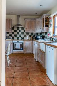 a kitchen with wooden cabinets and a tile floor at Cart Lodge - Holly Tree Barns in Halesworth