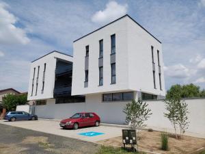 a white building with a red car parked in a parking lot at Casa Maria City Apartments in Timişoara