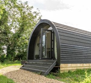 a small black house with an arched window and stairs at Glamping Pod One - Holly Tree Barns in Halesworth