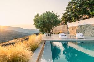 a swimming pool with two white chairs next to a mountain at Saffron Boutique in Krokos