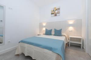 a white bedroom with a large bed with blue pillows at Victoria's Apartamentos in Málaga