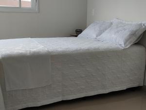 a white bed with white sheets and a window at Praia de Palmas - Lindo Apartamento in Governador Celso Ramos